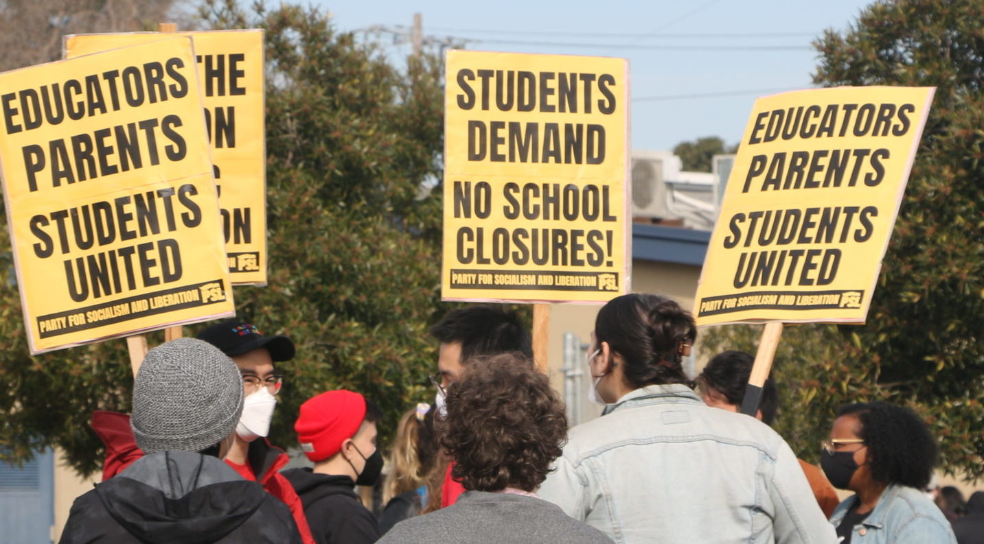 Protesters hold yellow signs reading 'Students demand no school closures!' and 'Educators, parents, students united.'