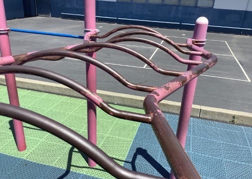 Rusted pink monkey bars on a school playground.