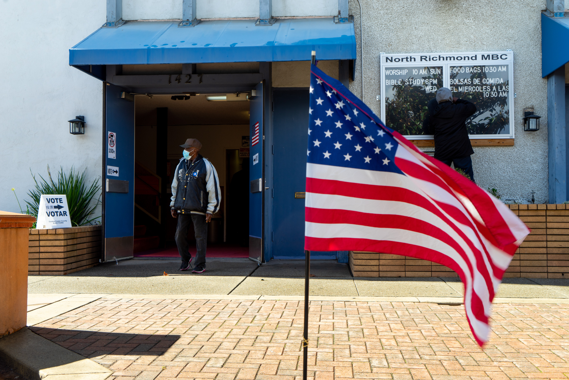 An American flag waves in front of a man exiting a polling station.