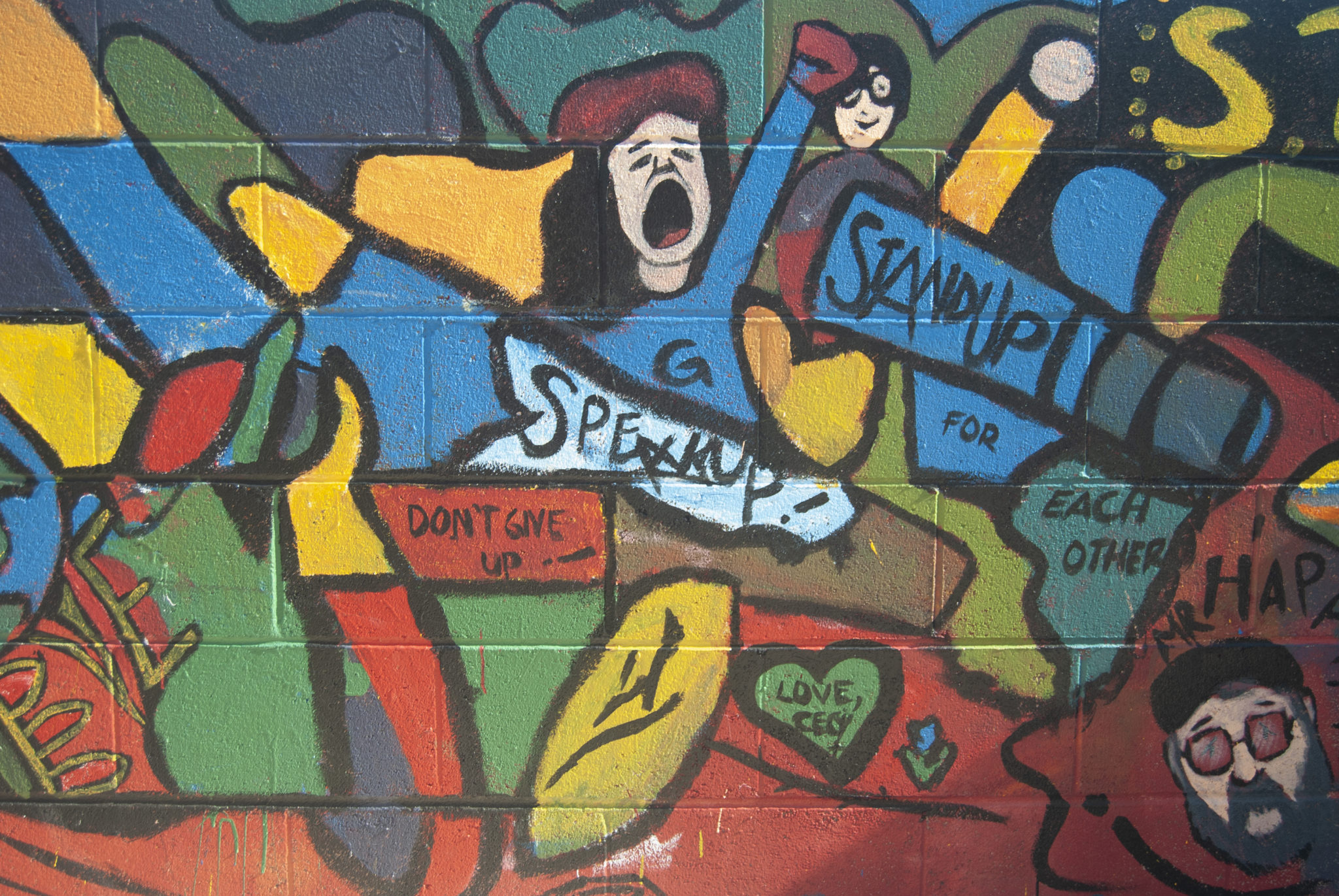 A colorful mural with a painted woman in the middle holding a raised fist and shouting 'Stand up!'