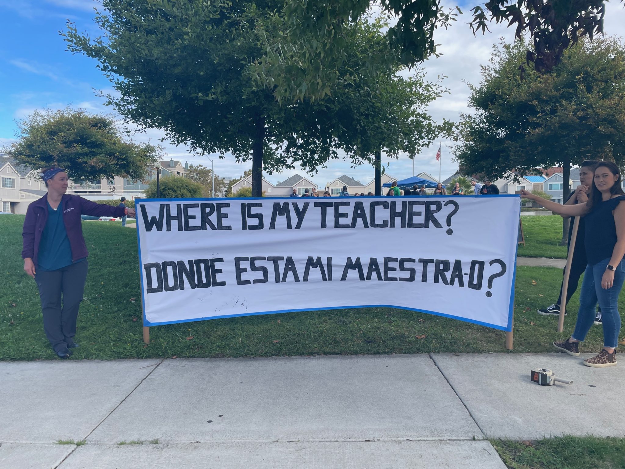 Parent protesters holding up a white sign reading 'Where's my teacher? Donde esta mi maestrao?'