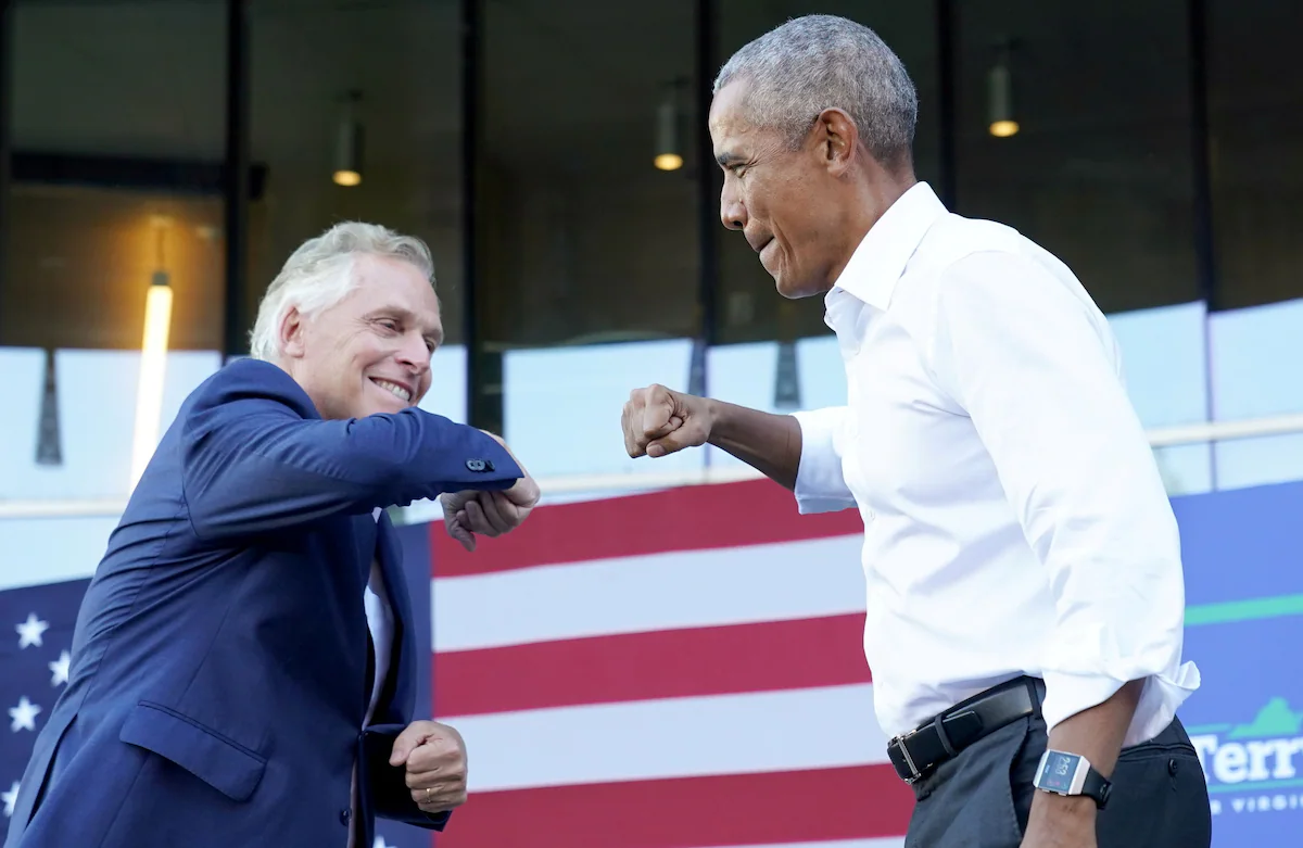 Terry McAuliffe and Barack Obama fist bump in front of an American flag.